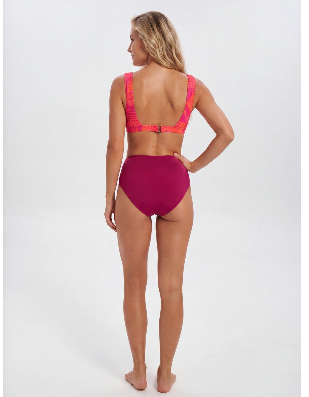 A woman modeling a two-piece bikini from the back, featuring a bright magenta high-waisted bottom and a matching magenta bikini top with neon pink straps, set against a plain white studio background. Sandbar Swimwear