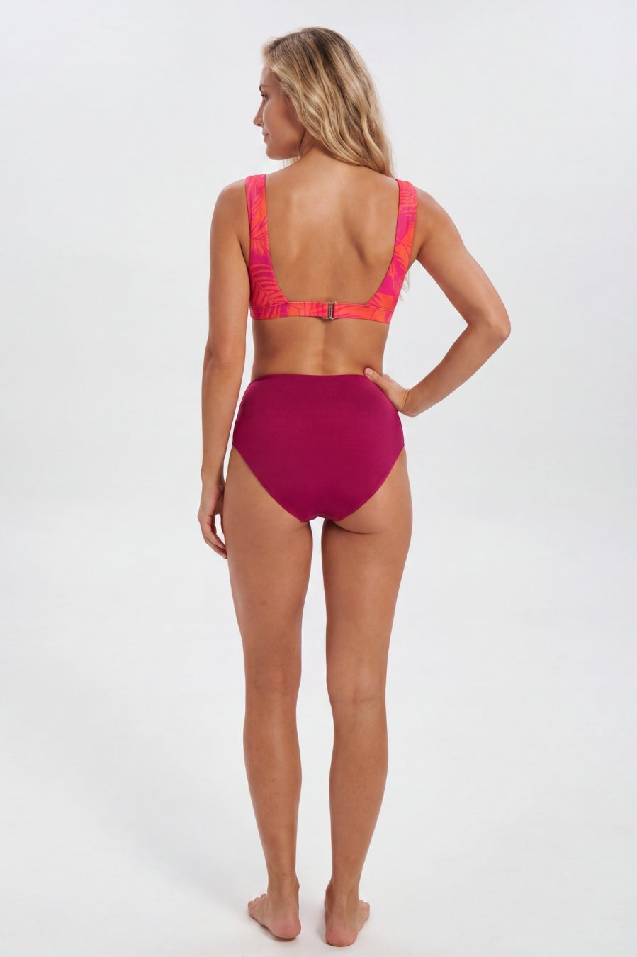 A woman modeling a two-piece bikini from the back, featuring a bright magenta high-waisted bottom and a matching magenta bikini top with neon pink straps, set against a plain white studio background. Sandbar Swimwear