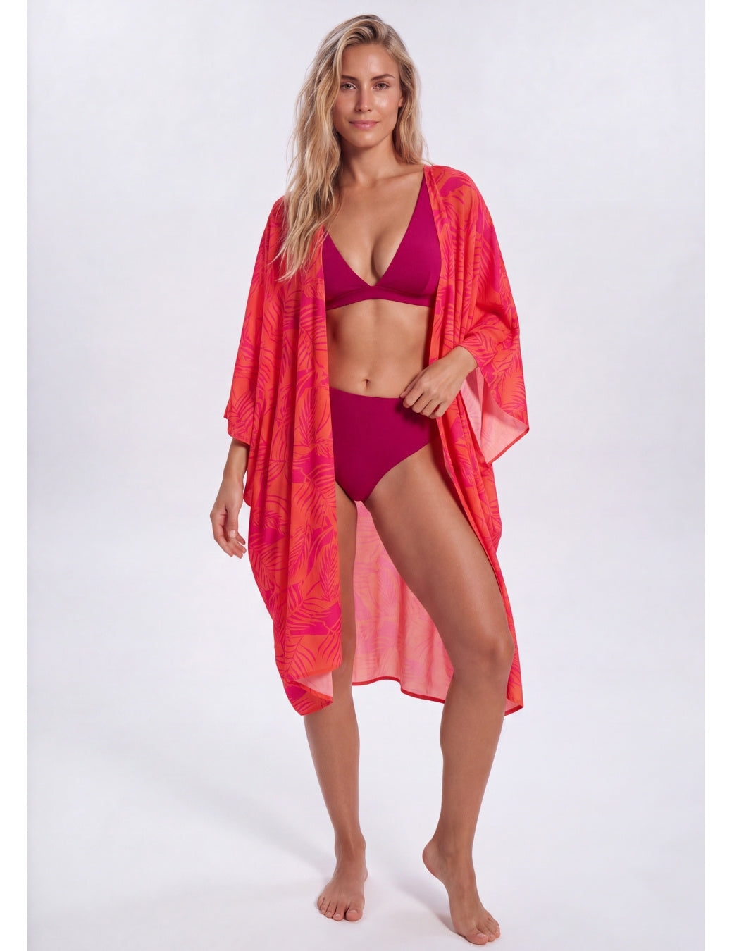Woman wearing the Aperol Palm caftan open over a plum bikini, full-length view