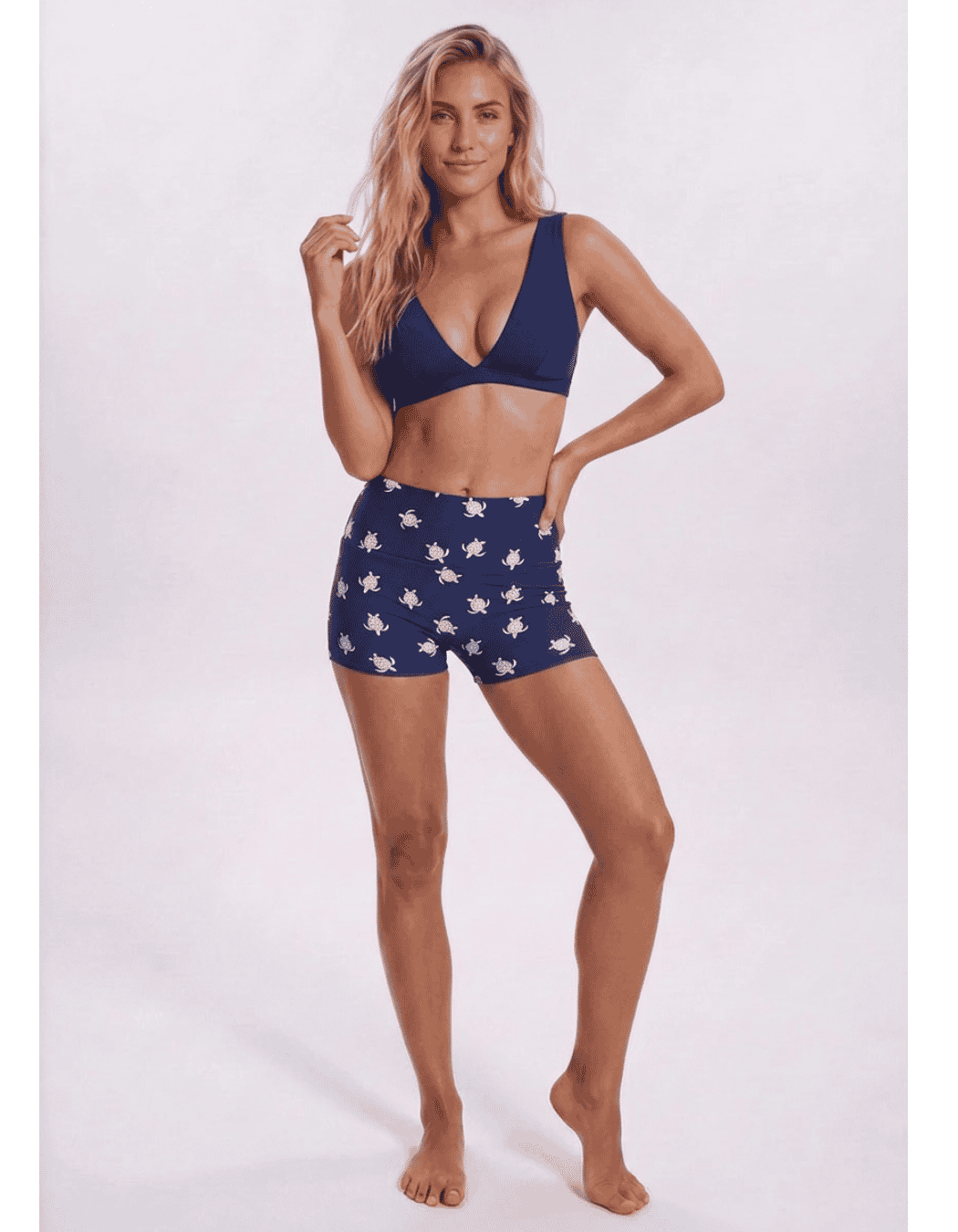 A woman modeling a matching two-piece swimsuit or lounge set with a navy blue triangle bikini top and matching shorts featuring a white star pattern, set against a plain light gray studio background. Sandbar Swimwear
