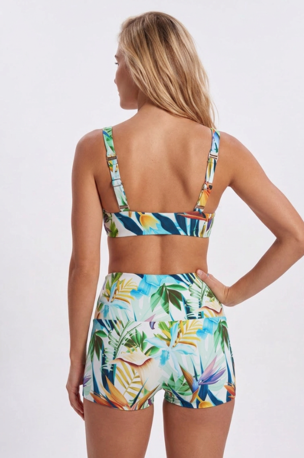A woman shown from the back wearing a matching tropical print bikini set with a sports bra top and high-waisted shorts, against a light gray studio background. Sandbar Swimwear