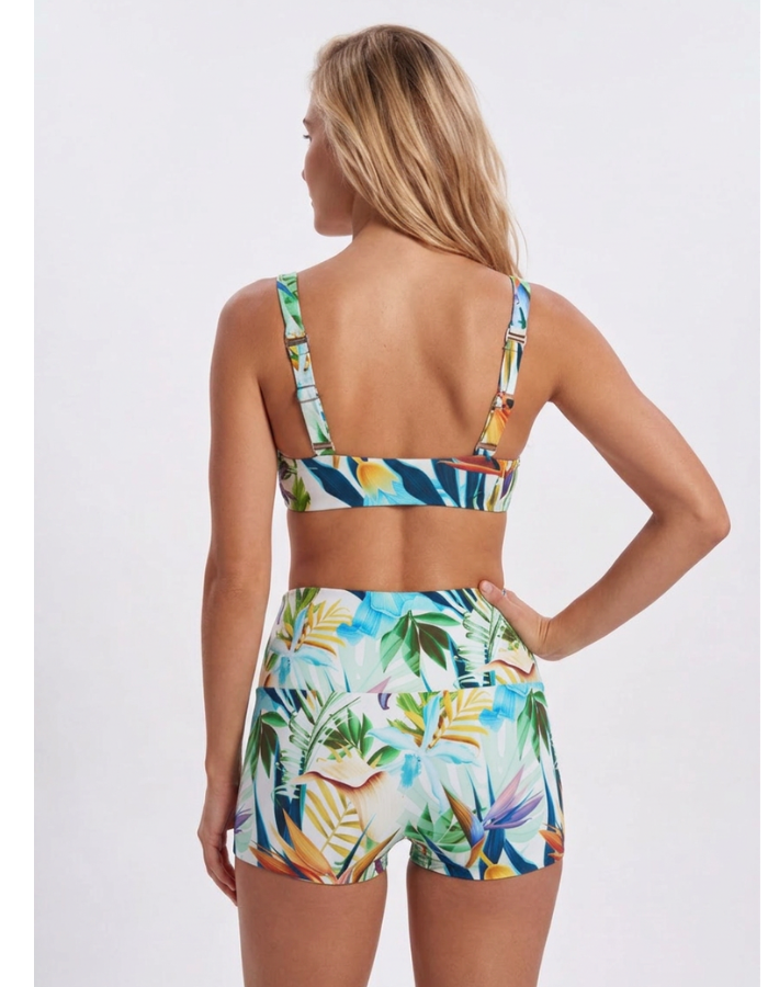 A woman shown from the back wearing a matching tropical print bikini set with a sports bra top and high-waisted shorts, against a light gray studio background. Sandbar Swimwear