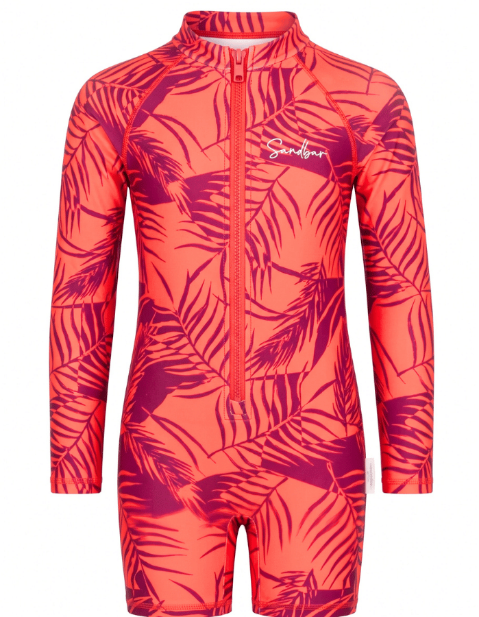 A long-sleeve, one-piece children's swim suit featuring a vibrant coral pink and magenta tropical palm leaf pattern, with a front zipper and a white 'Sandbar' brand logo on the chest.