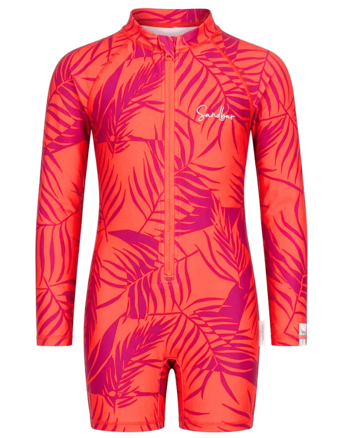 A girls' long-sleeve one-piece swimsuit with a bright coral-orange base and a magenta tropical leaf print, featuring a front zipper and a white script logo on the chest.