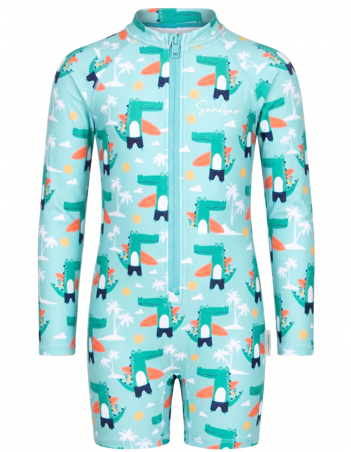 A children's long-sleeve one-piece swimsuit or sun protection suit in light aqua, featuring a repeating cartoon dinosaur pattern with surfboards, palm trees, and small yellow circles, plus a front zipper.