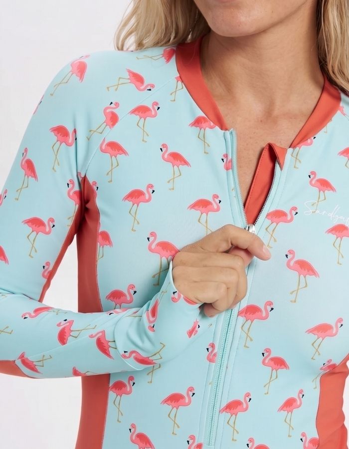 A close-up of a woman wearing a light blue long-sleeve zip-up top with a pink flamingo print and coral orange trim.