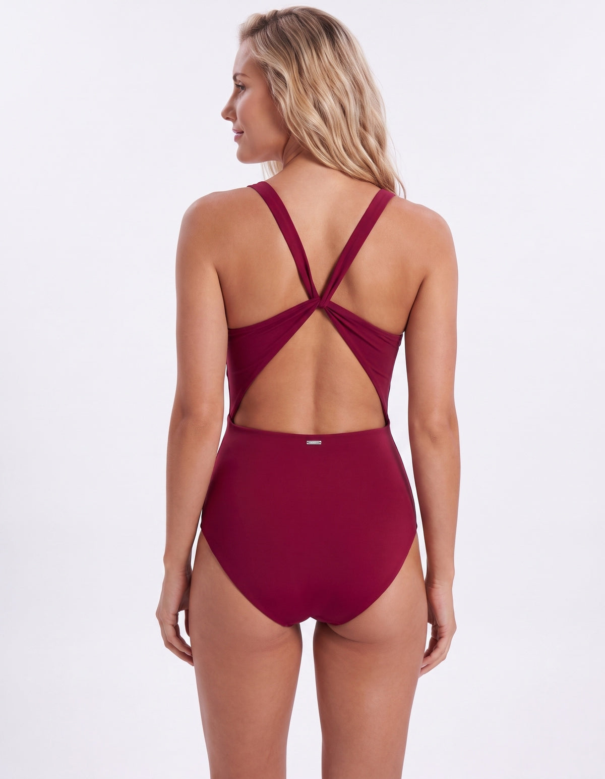 A woman modeling a high-waisted one-piece swimsuit from the back, showing a crossover criss-cross strap design and a solid deep burgundy color, set against a plain white studio background.
