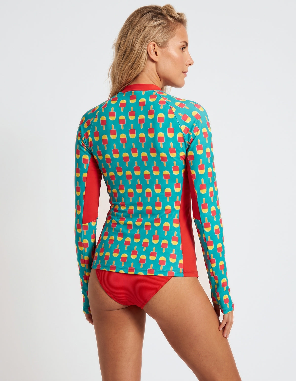 A woman modeling a long-sleeve swim top from the back, featuring a turquoise background with a repeating red and yellow ice cream cone pattern and solid red side panels and bikini bottom.