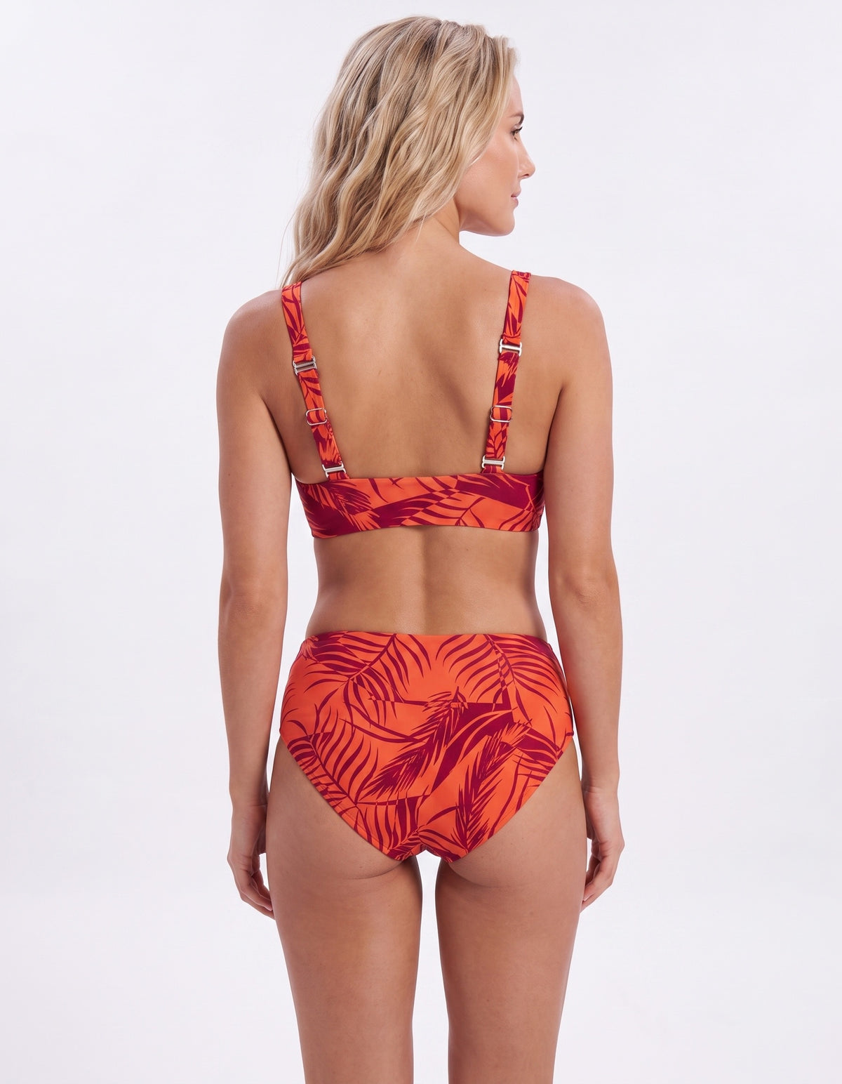A woman shown from the back wearing a two-piece bikini with a red and orange tropical leaf print, set against a plain white studio background.