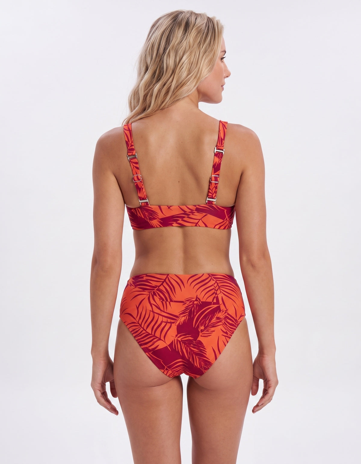 A woman shown from the back wearing a two-piece bikini with a red and orange tropical leaf print, set against a plain white studio background.