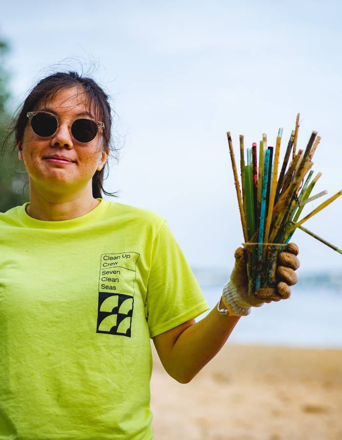 Seven Clean Seas team member holding plastic straws collected during a beach clean-up
