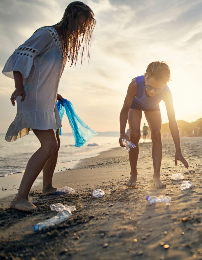 A mother and daughter collecting plastic bottles from a beach at sunset