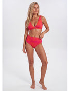 A woman modeling a two-piece bikini swimsuit with a bright pink and orange abstract pattern against a plain light gray studio background. Sandbar Swimwear