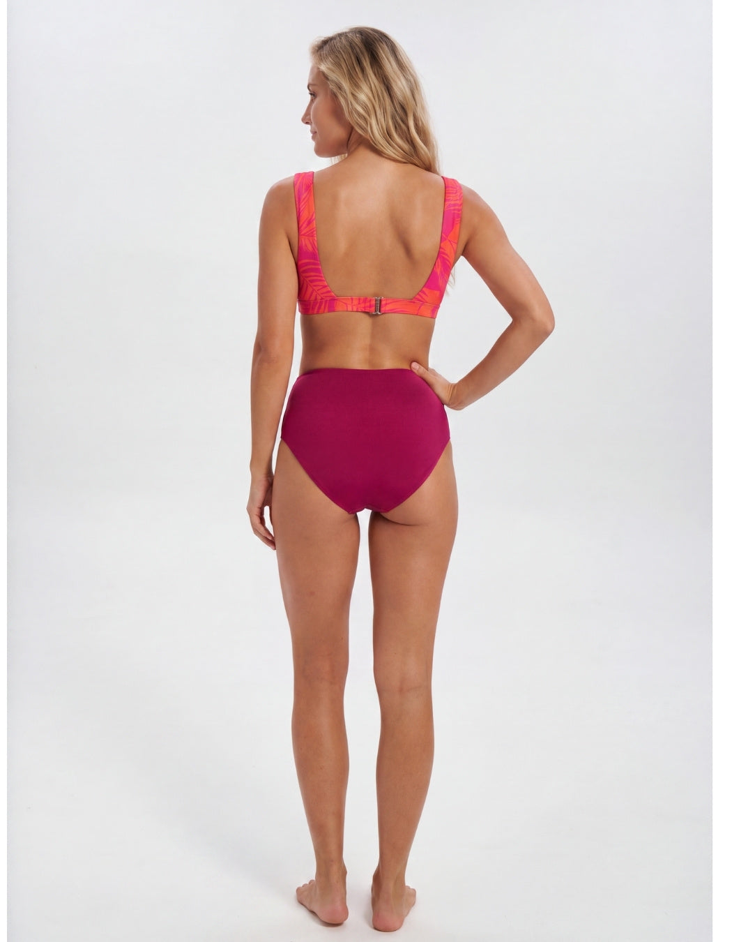 A woman modeling a two-piece bikini from the back, featuring a bright magenta high-waisted bottom and a matching magenta bikini top with neon pink straps, set against a plain white studio background. Sandbar Swimwear