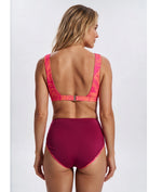 A woman shown from the back wearing a two-piece swimsuit with a bright pink and orange abstract patterned bra top and high-waisted magenta bottoms, against a light gray studio background. Sandbar Swimwear