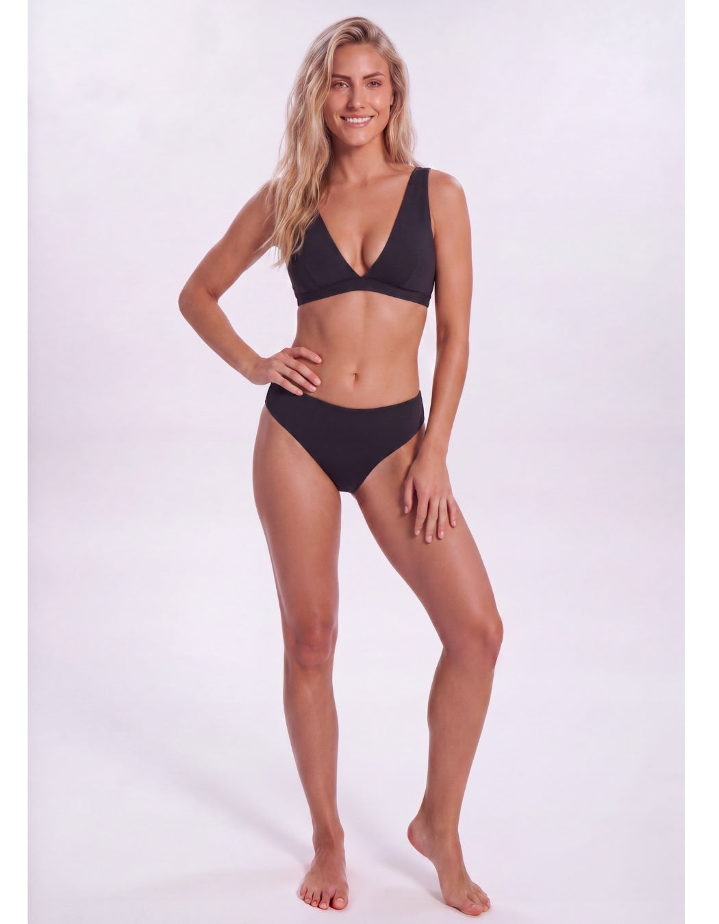A woman modeling a two-piece bikini set in a solid black color, standing against a plain light gray studio background. Sandbar Swimwear