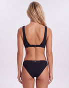 A woman shown from the back wearing a black two-piece bikini against a plain light gray studio background. Sandbar Swimwear