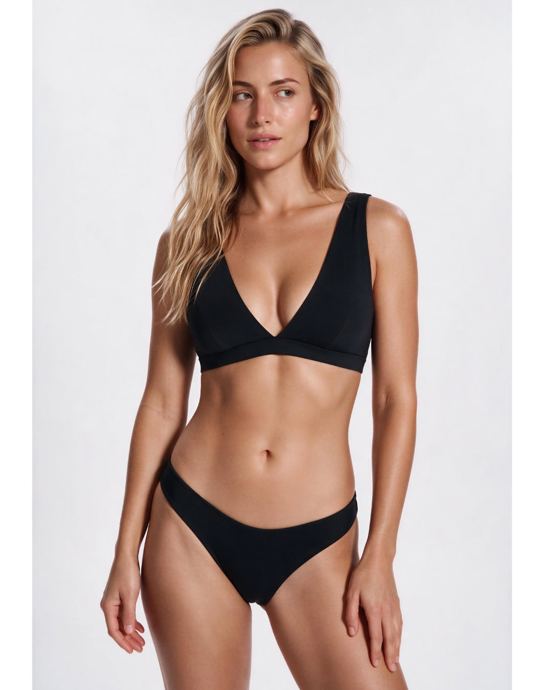 A woman modeling a black two-piece bikini set against a plain light gray studio background. Sandbar Swimwear