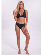 A woman modeling a two-piece black bikini against a plain light gray studio background. Sandbar Swimwear