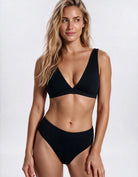 A woman modeling a black two-piece bikini set against a plain light gray studio background. Sandbar Swimwear