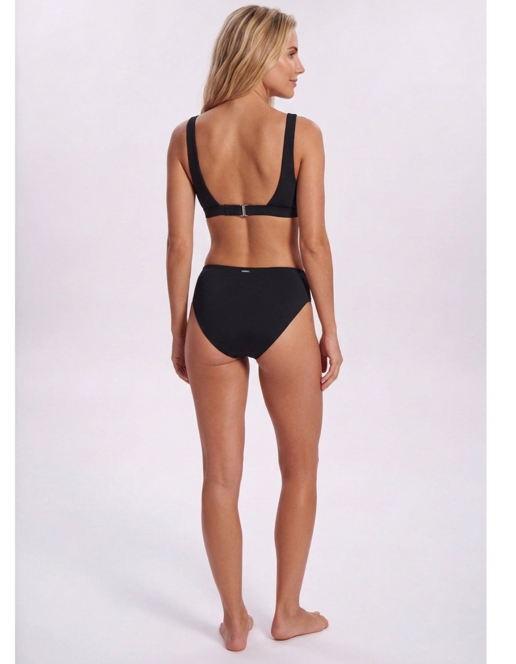 A woman modeling a black two-piece bikini from the back, showing the open back design and high-waisted bottoms, against a plain light background. Sandbar Swimwear