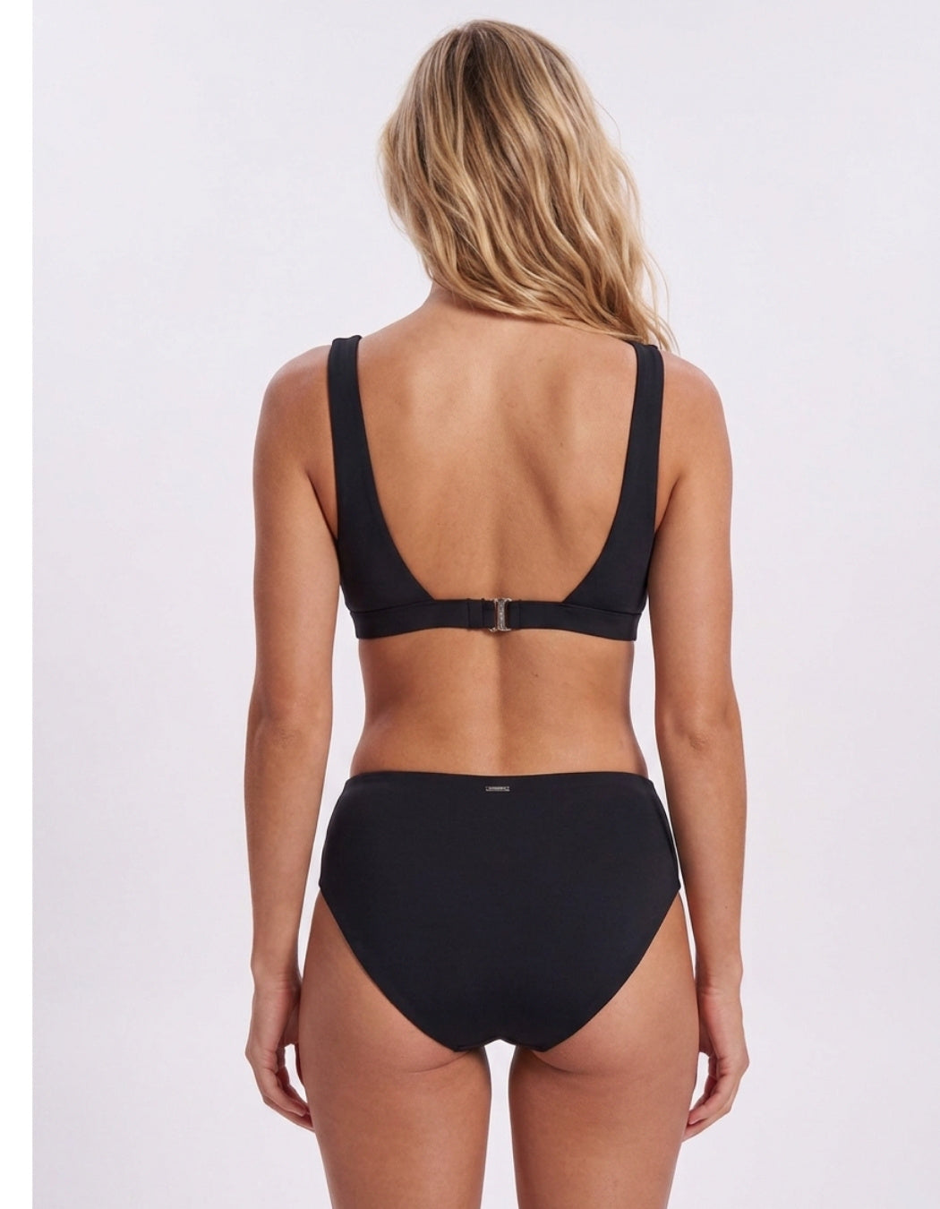 A woman shown from the back wearing a black two-piece bikini with a scoop neckline and high-waisted bottoms, photographed against a plain light gray studio background. Sandbar Swimwear