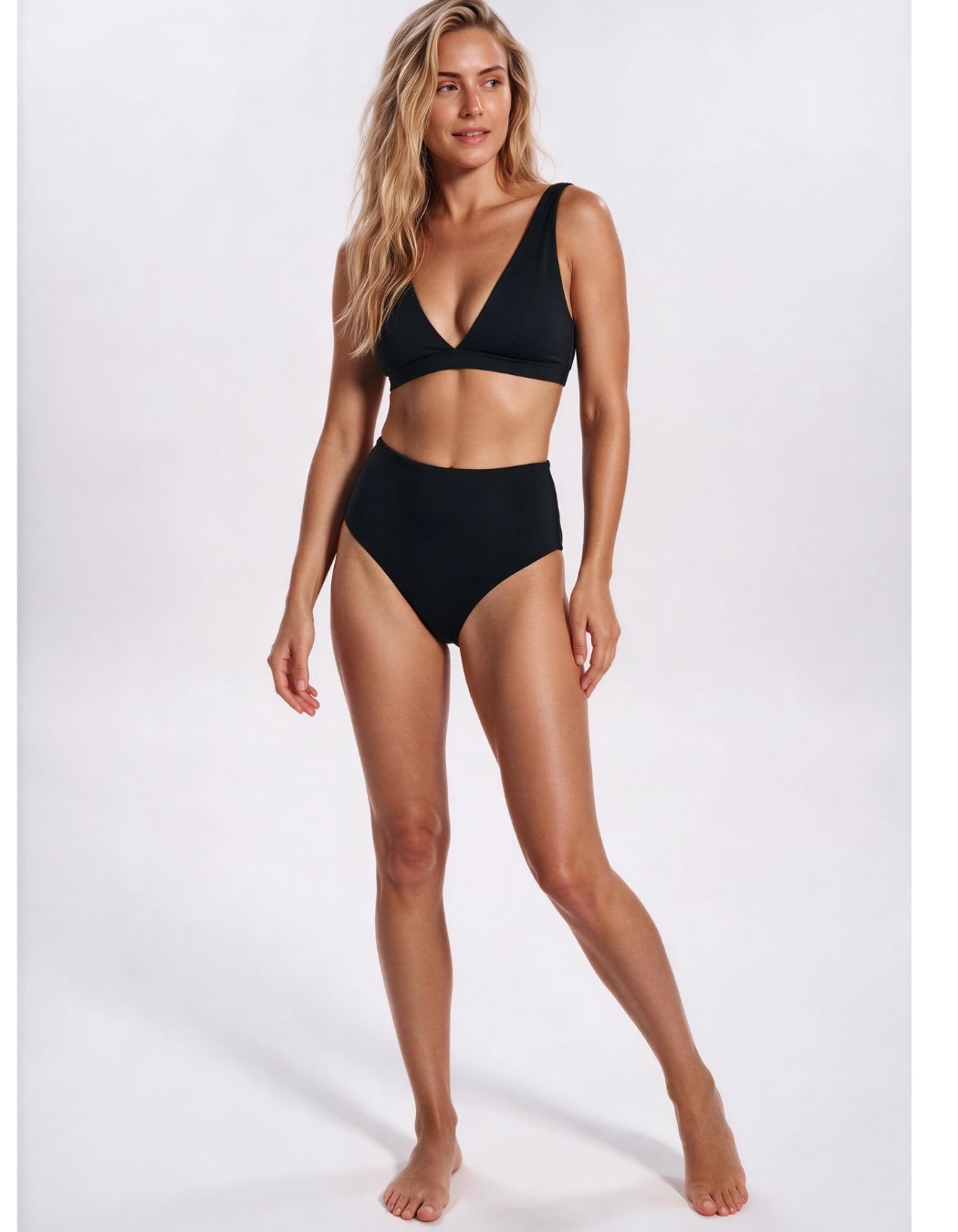 A woman modeling a solid black two-piece bikini set against a clean, light gray studio background. Sandbar Swimwear