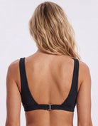 Rear view of a woman wearing a black bikini top with a low open back and a small silver buckle detail at the center, set against a plain light gray background. Sandbar Swimwear