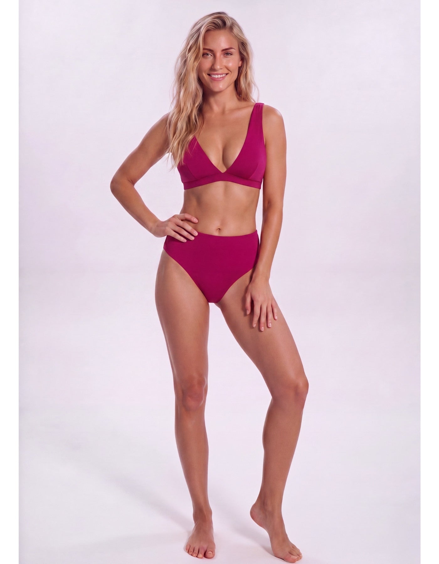 A woman modeling a two-piece bikini in a deep magenta color against a plain white studio background.Sandbar Swimwear
