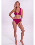 A woman modeling a two-piece bikini in a deep magenta color against a plain white studio background.Sandbar Swimwear