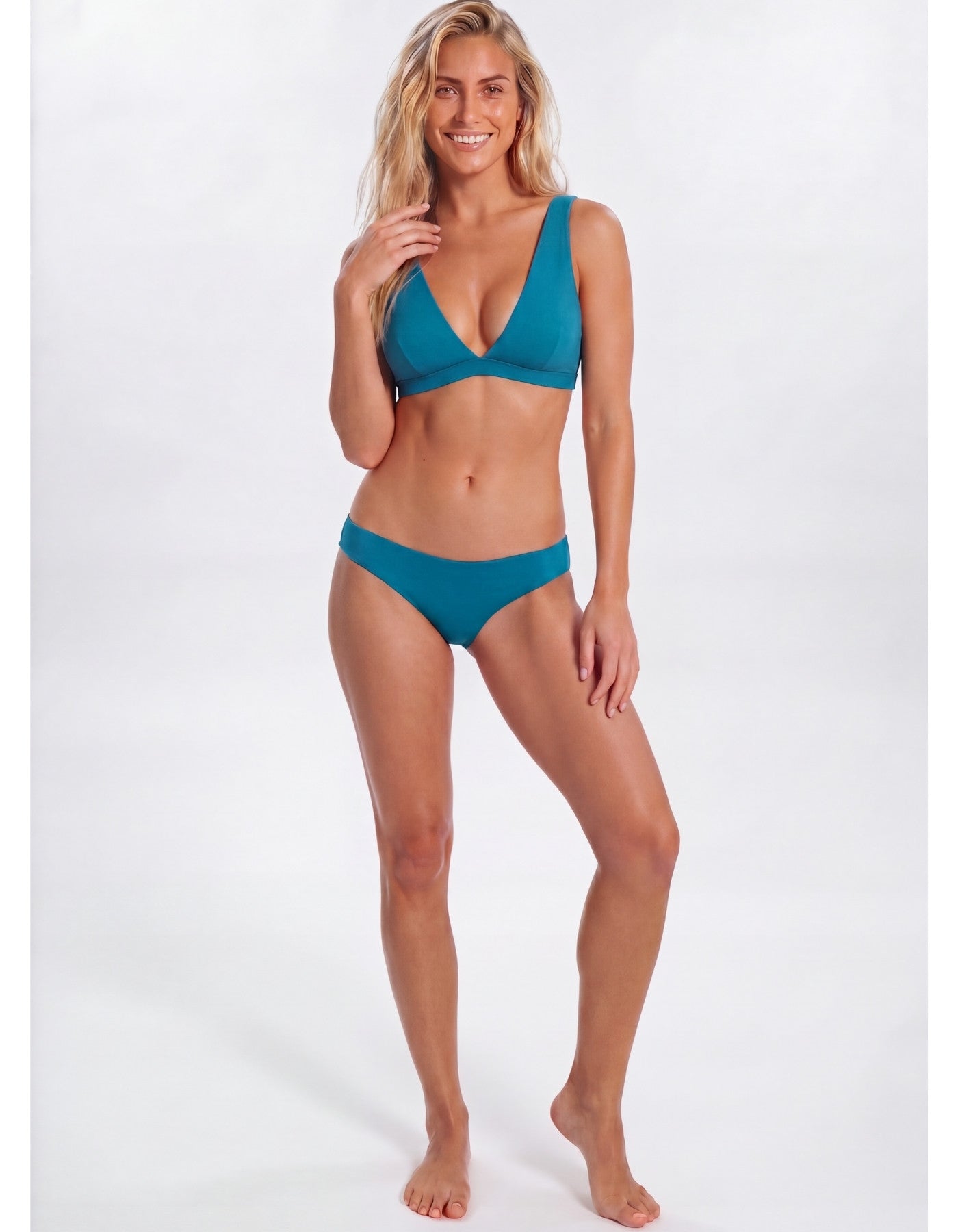 A woman modeling a two-piece bikini in a solid teal color, standing against a plain white studio background Sandbar Sustainable Swimwear