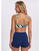 A woman shown from the back wearing a two-piece swimsuit with a tropical floral print bikini top and solid navy blue high-waisted shorts, against a light gray studio background. Sandbar Swimwear