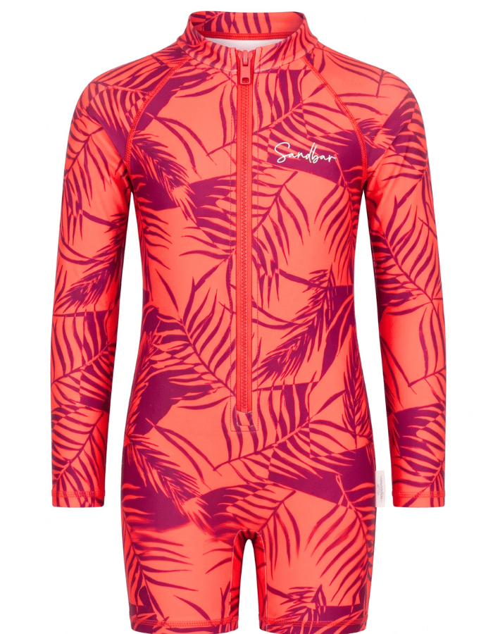 A long-sleeve, one-piece children's swim suit featuring a vibrant coral pink and magenta tropical palm leaf pattern, with a front zipper and a white 'Sandbar' brand logo on the chest.