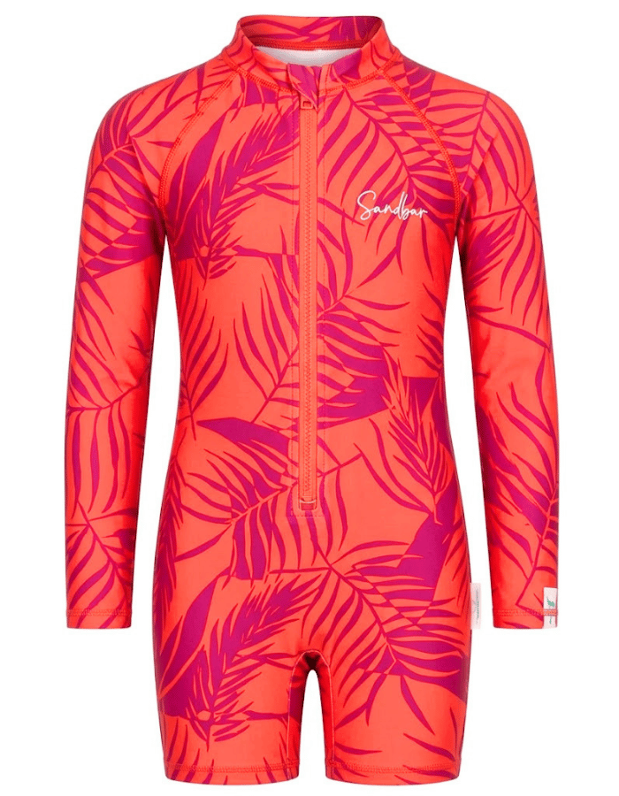 A girls' long-sleeve one-piece swimsuit with a bright coral-orange base and a magenta tropical leaf print, featuring a front zipper and a white script logo on the chest.