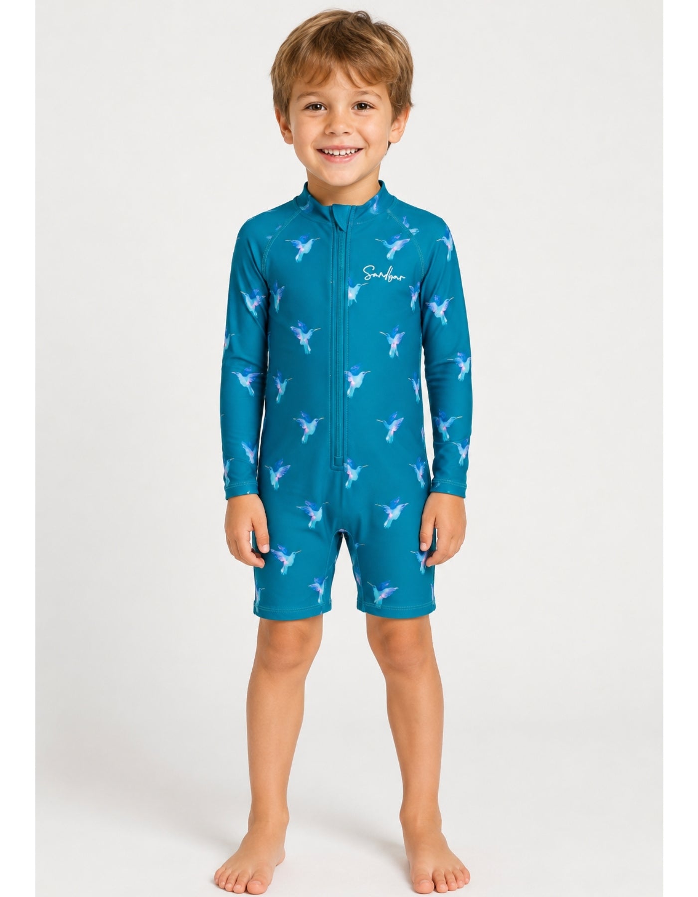 A young boy wearing a teal blue full-body swim suit with a white bird pattern, standing against a light gray studio background.