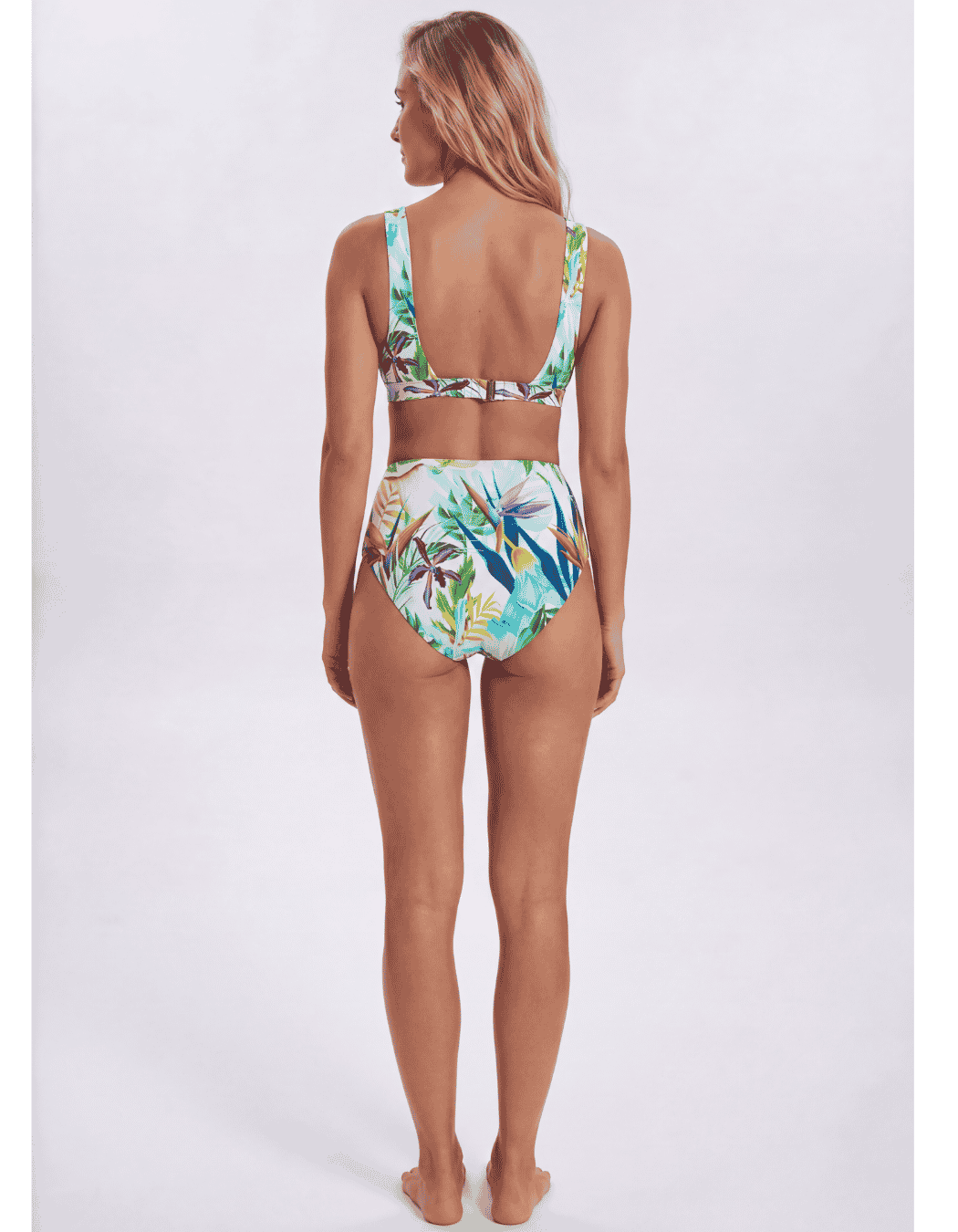 A woman shown from the back wearing a two-piece bikini with a tropical leaf print, featuring a halter-style top and high-waisted bottoms, against a light gray studio background. Sandbar Swimwear