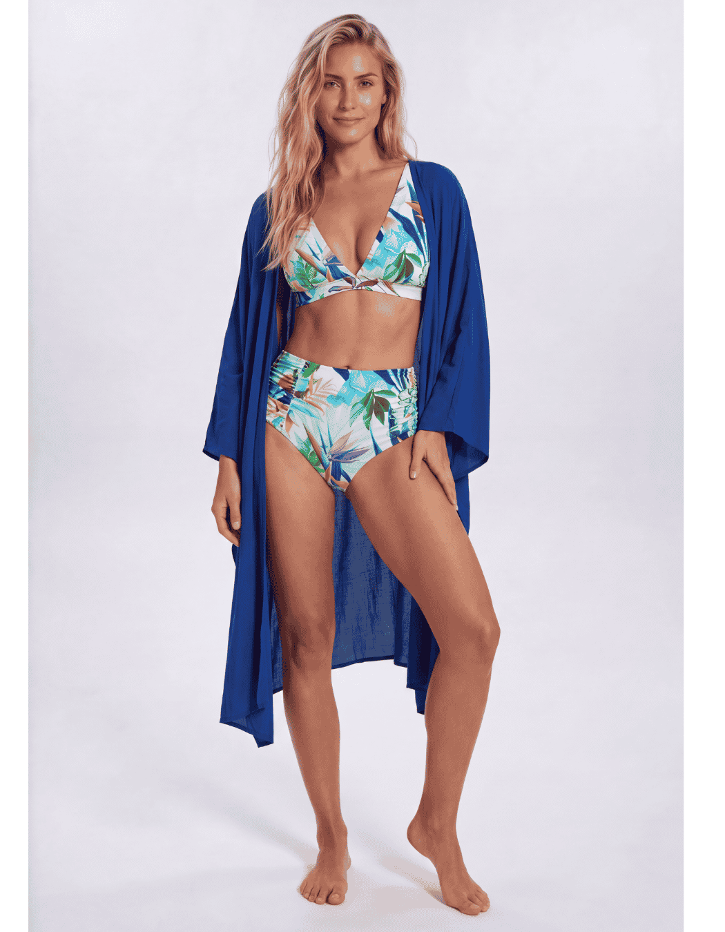 A woman modeling a tropical print two-piece bikini with a matching open-front blue cover-up cardigan, standing against a light gray studio background. Sandbar Swimwear 