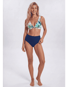 A woman modeling a two-piece bikini against a plain light gray studio background. The bikini top has a tropical leaf print in green, blue, and white, while the high-waisted bottoms are solid navy blue. Sandbar Swimwear