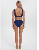 A woman viewed from the back wearing a navy blue two-piece bikini against a plain light gray studio background. Sandbar Swimwear