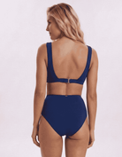 A woman shown from the back wearing a navy blue two-piece swimsuit with a high-waisted bottom and a scoop-style open back top, photographed against a plain light background. Sandbar Swimwear
