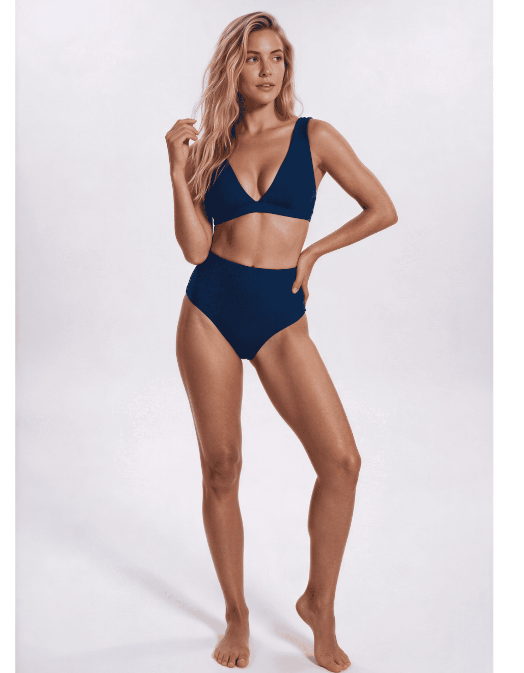 A woman modeling a two-piece navy blue bikini against a plain light gray studio background. Sandbar Swimwear