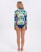 A woman shown from the back wearing a long-sleeve swim rash guard with a colorful tropical bird and floral print, paired with navy blue bikini bottoms, against a plain white studio background.