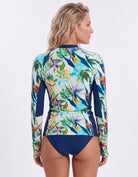 A woman shown from the back wearing a long-sleeve swim rash guard with a tropical floral print and solid navy blue side panels and bottom, against a light gray studio background.