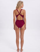 A woman shown from the back wearing a one-piece swimsuit in deep burgundy, featuring a high-cut bottom and an open crisscross back design, set against a plain white studio background.