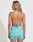 A woman shown from the back wearing a turquoise and white tropical leaf print halter bikini top and matching high-waisted shorts against a plain white studio background.
