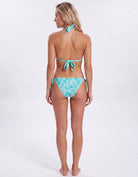 A woman modeling a two-piece bikini from the back, featuring a turquoise and white tropical leaf pattern. The bikini includes a tie-shoulder top and matching side-tie bottoms, shown against a plain white studio background.
