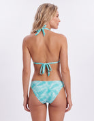 A woman shown from the back wearing a turquoise and white palm-leaf print bikini with tie straps at the back, photographed against a clean white studio background.