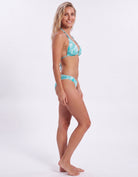 A woman modeling a two-piece bikini with a turquoise and white abstract pattern against a plain white studio background.