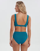 A woman shown from the back wearing a teal two-piece swimsuit with a scoop back and high-waisted bottoms, photographed against a light gray studio background.
