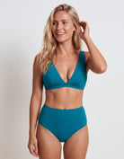 A woman modeling a two-piece teal bikini against a light gray studio background. The set includes a wrap-style triangle bikini top and high-waisted bikini bottoms.